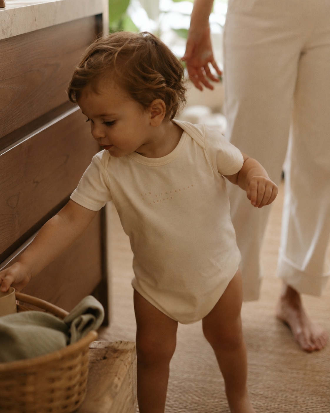 Baby in funny printed bodysuit in warm home setting — natural light, real life context, wearable beyond the photo moment