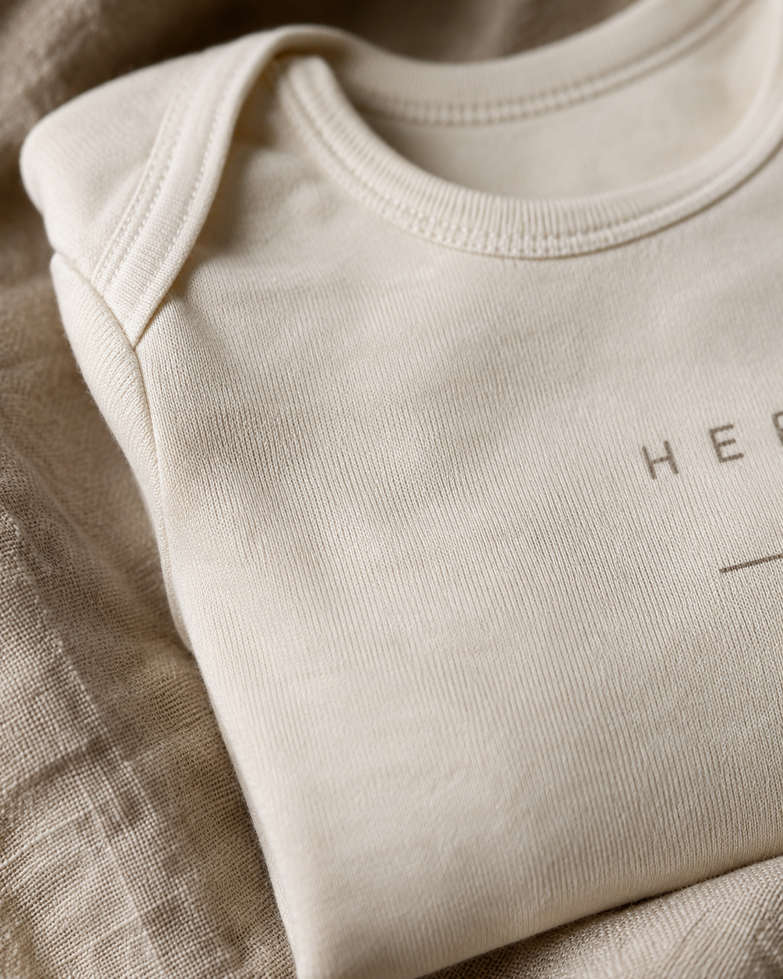 Close detail of a funny baby bodysuit showing clean typography on soft cream fabric — clever, not loud